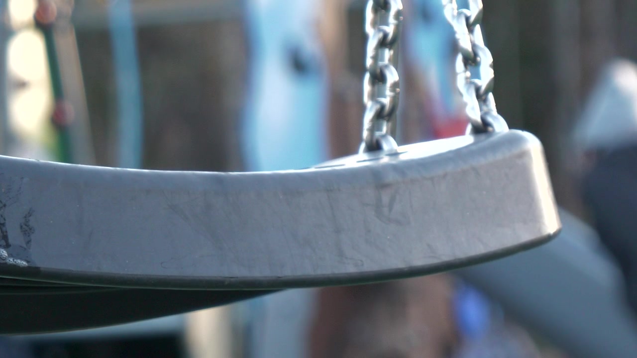 Risco de infecção em parque infantil, saliva no balanço e pessoas em segundo plano desfocado, em câmera lenta estática.