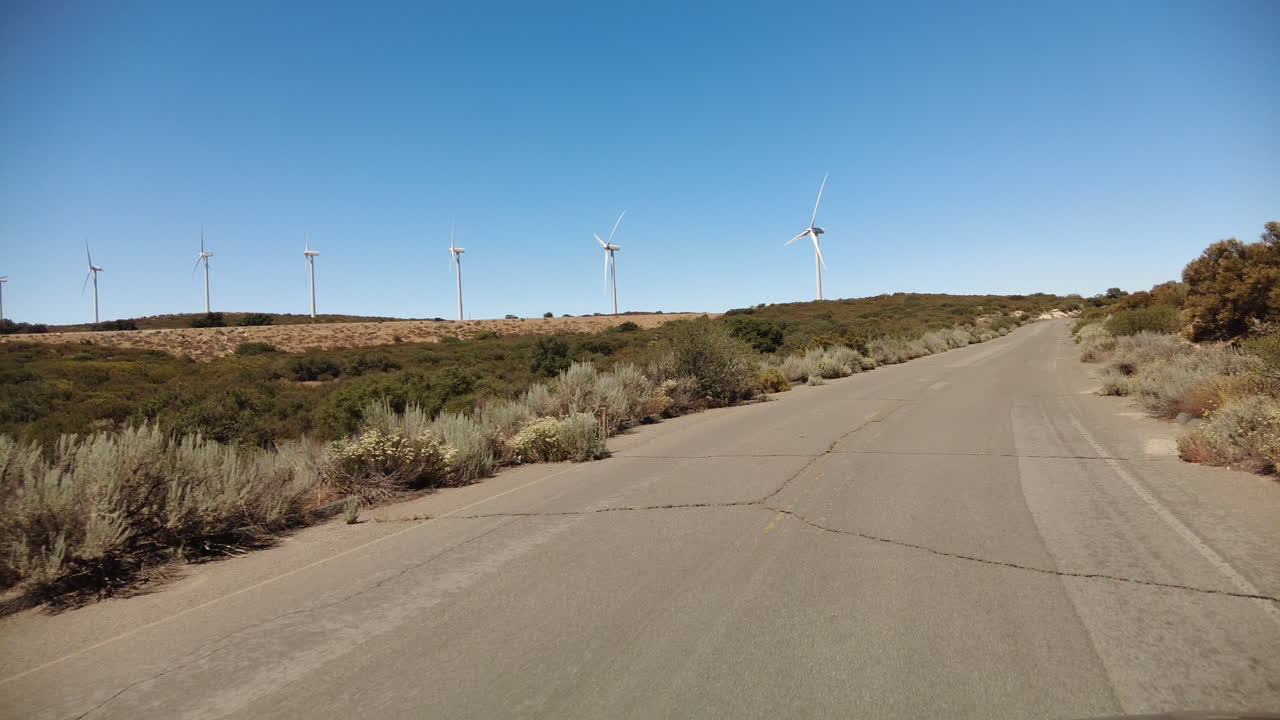Driving on road towards freeway and wind turbines on a hill, California