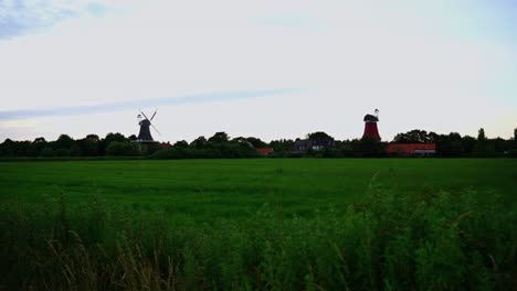Alte-Schöne-Windmühlen-Mit-Einem-Kleinen-Dorf-Hinter-Einem-Feld-In-Der-Sonne