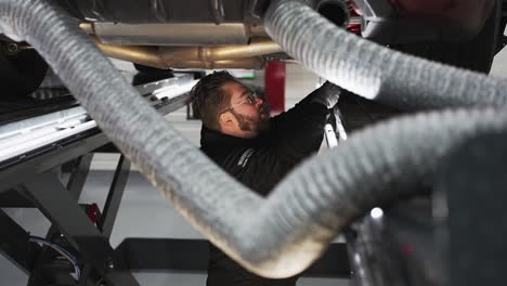 car mechanic in a workshop working on a passenger vehicle under the car