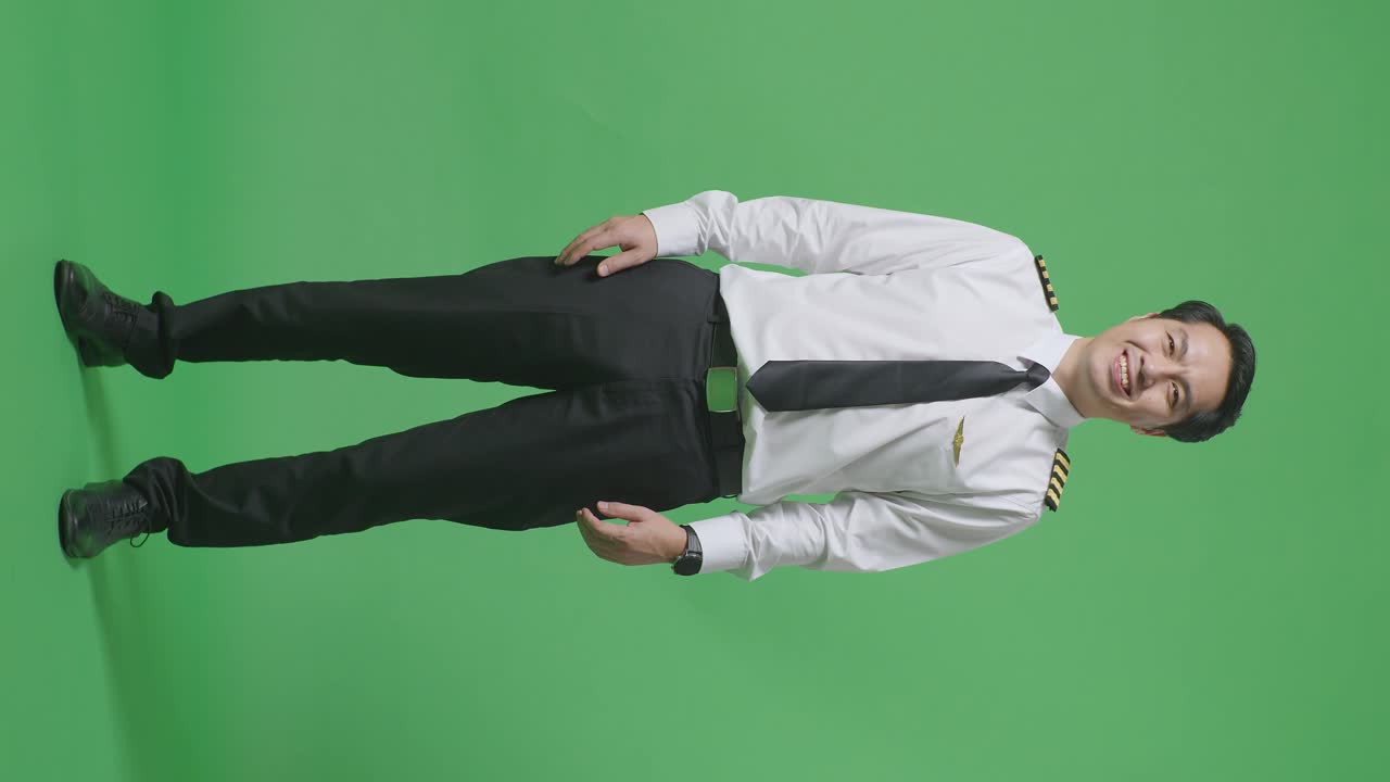 녹색 스크린 배경 스튜디오에서 카메라에 서서 미소 짓는 아시아 남성 조종사의 몸이 가득 차 있습니다.