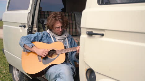 a young guy with glasses plays the guitar in the back of a caravan