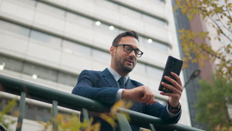 businessman talking in video call using mobile phone at urban city street leaning on railing