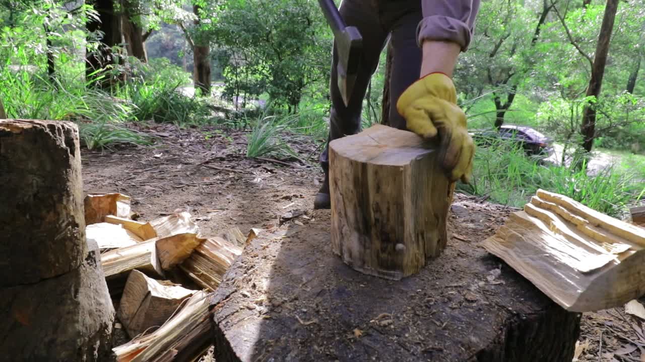 통나무에서 도끼를 뽑은 다음 겨울 연료를 위해 쪼개고, 뒤에 있는 녹색 초목 - 통나무, 다리, 작업 부츠 및 작업 장갑 닫기 - 슬로우 모션