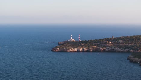 Far-aerial-view-of-lighthouse-near-blue-water-limestone-shore,-Mallorca