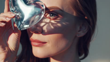 close-up portrait of a woman holding a crystal heart, reflecting sunlight onto her face