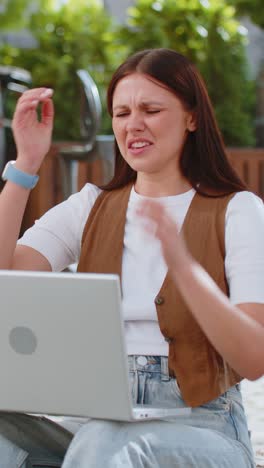 Caucasian young woman using laptop browsing loses lottery results bad news sitting in city street