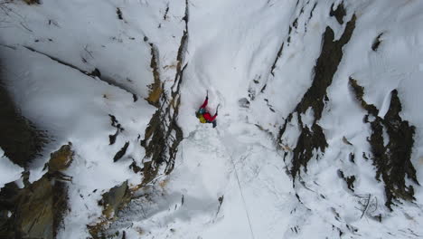 Disparo-De-Drone-Mientras-Nieva-En-El-Paisaje-Del-Circuito-De-Annapurna-En-Nepal,-Un-Montañero-Sube-Una-Montaña-Y-Una-Cascada-Congelada,-Una-Experiencia-Turística-Aventurera-Y-Peligrosa-4k