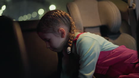 a close view of a child turning on the light in a car, reaching up towards the ceiling light with a focused expression, as if searching for something