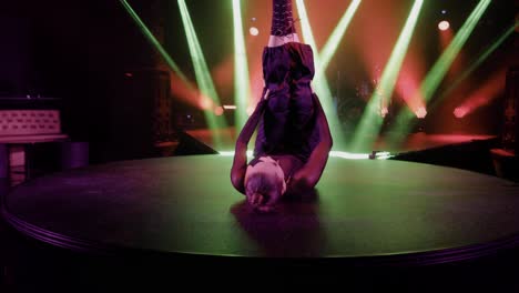 in the club, a girl lying on the stage dances under concert lights, wearing black pants and a top with a long braid