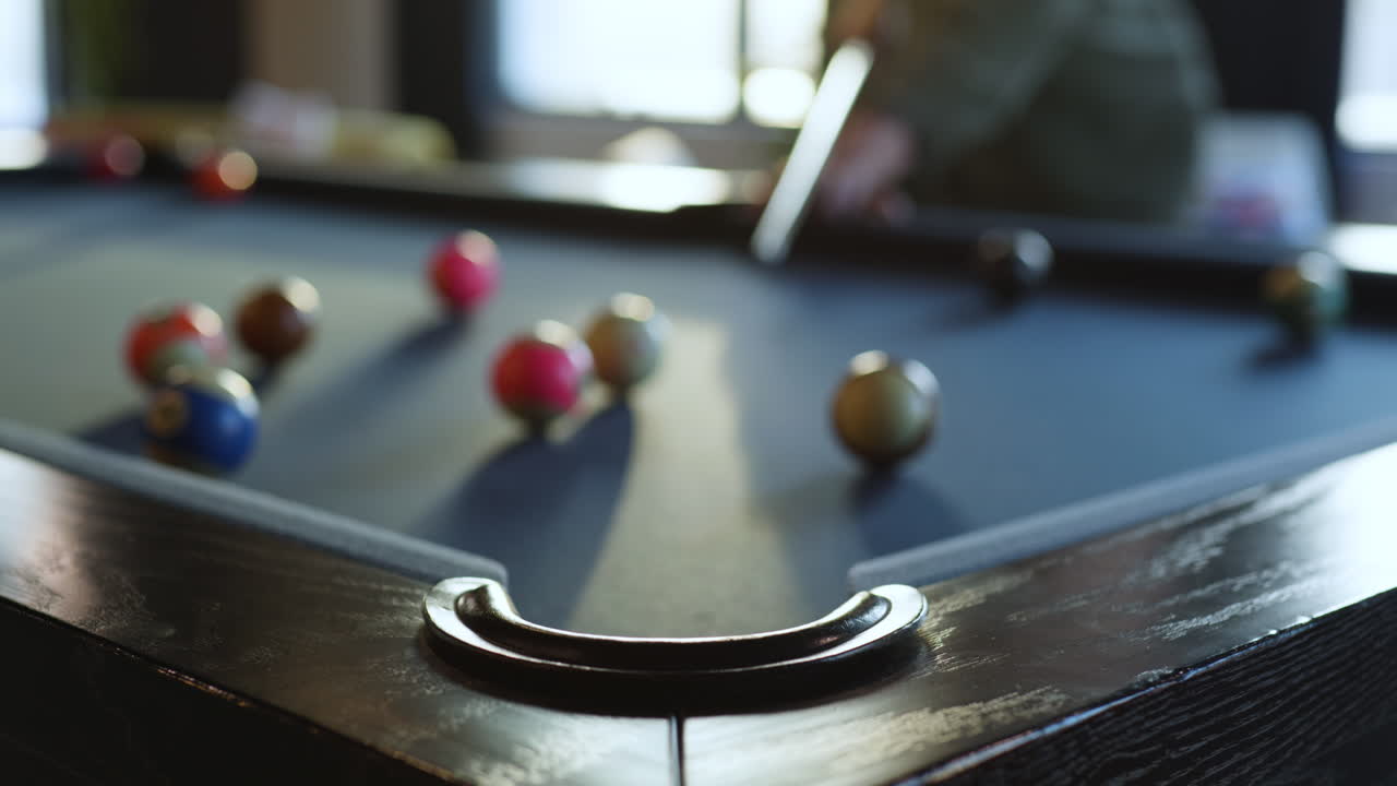 A person takes a shot at a billiards table filled with colorful balls in a bright indoor setting. The atmosphere is relaxed, showcasing an engaging social activity.
