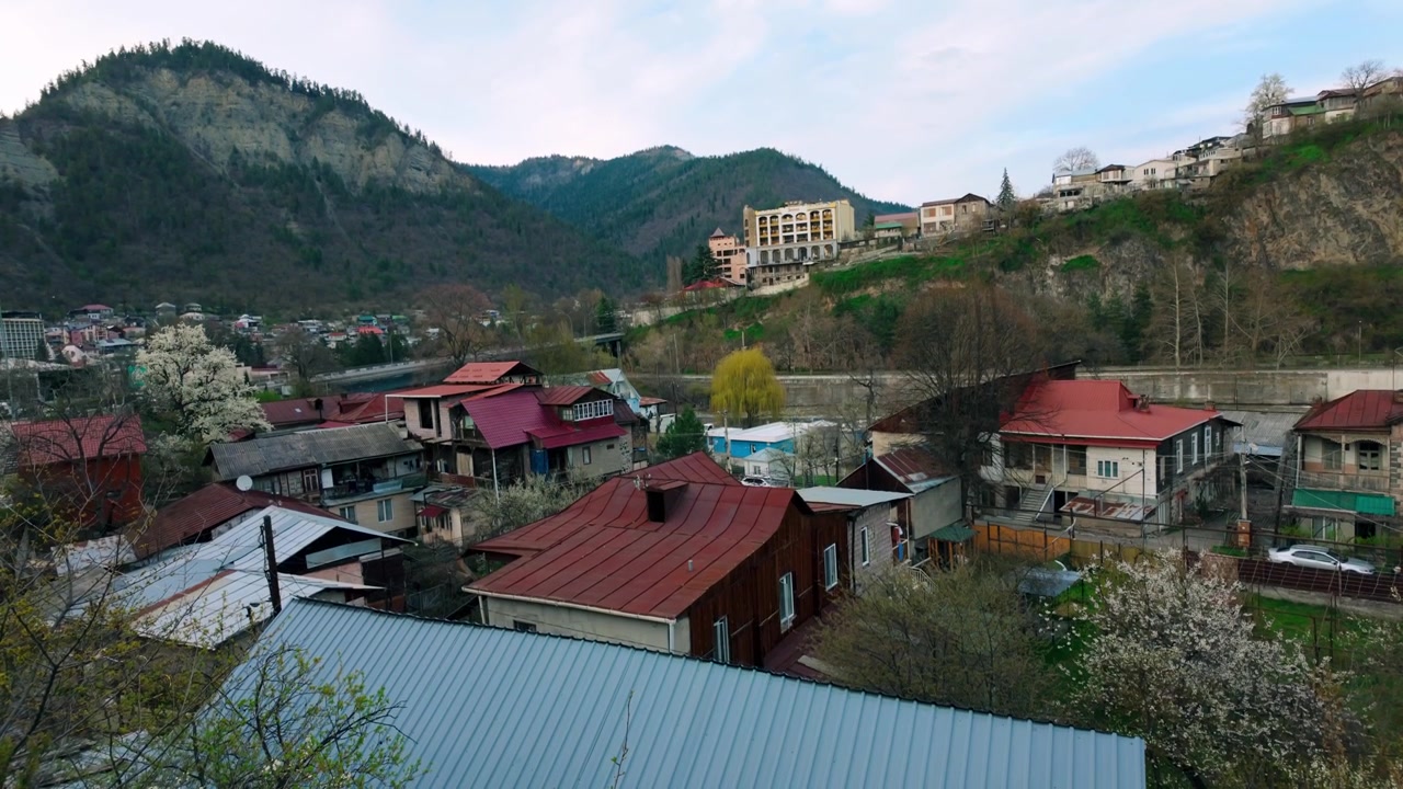 Gürcistan'ın Borjomi vadisine kurulmuş, karakteristik kırmızı çatılı konutların havadan görünümü. Binalar manzara boyunca dağınık bir şekilde yer alıyor, içinden bir nehir akıyor ve heybetli yeşil dağlar...