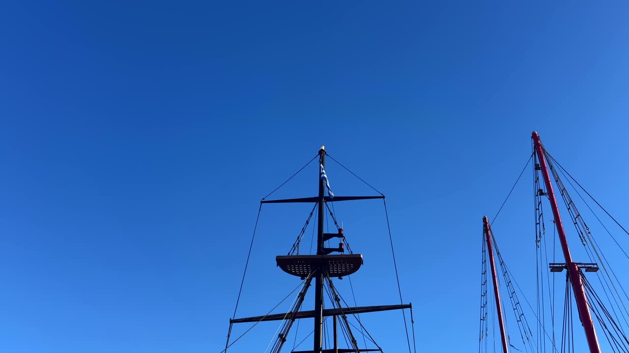 Tall sailboat masts with rigging and a Greek flag against a clear blue sky at Crete Island, Greece