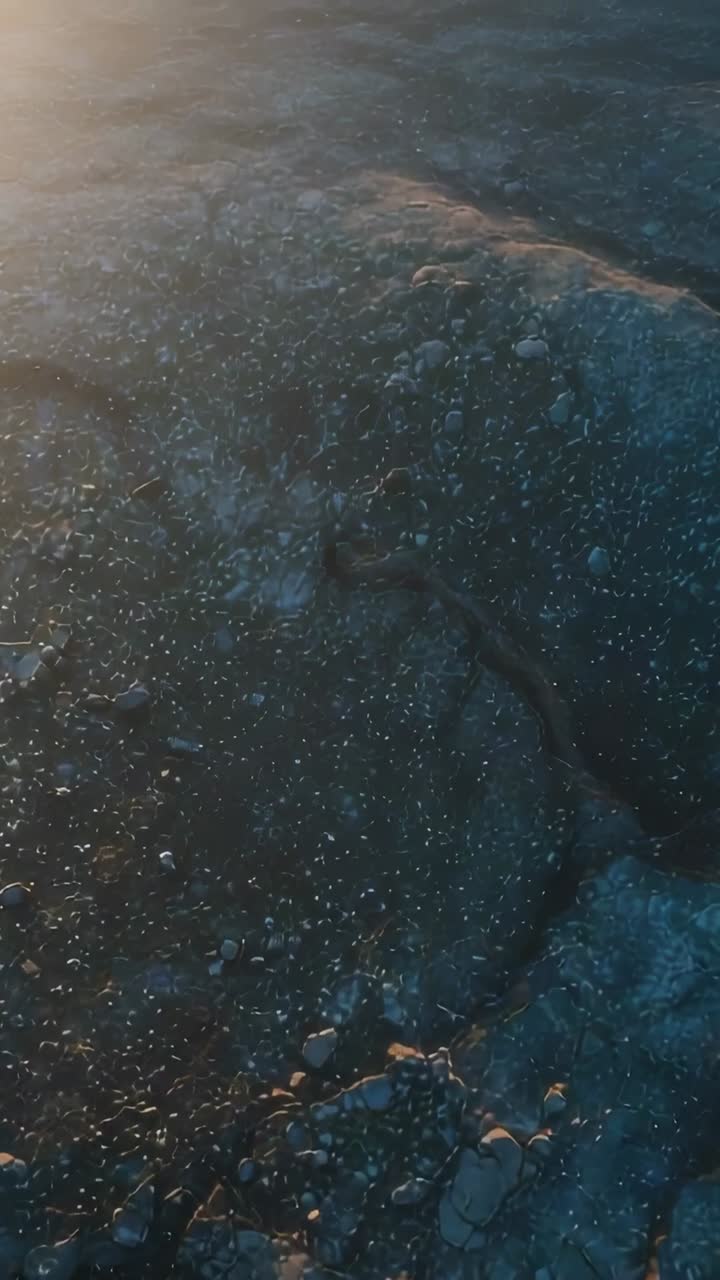Vertical video: Drone panning over cracked rock while low sun intensifying, showing stones, sheen