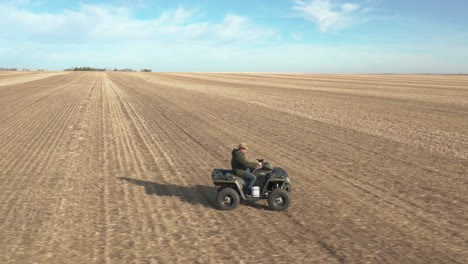 hombre conduciendo con atv en vastos campos agrícolas, seguimiento lateral aéreo