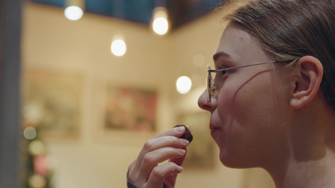 Young woman tasting. Indoor cafe with warm lighting ambiance. Female exploring delicacy in comfortable artistic space. Elegant young woman relishing rich flavors in cozy gallery cafe setting