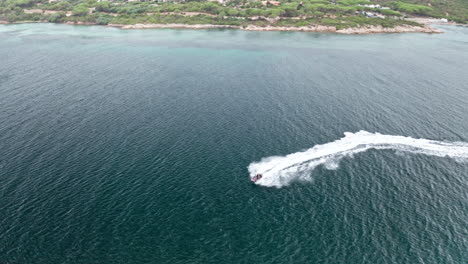 A-speedboat-cruising-near-the-sardinian-coastline,-showcasing-clear-blue-waters,-aerial-view