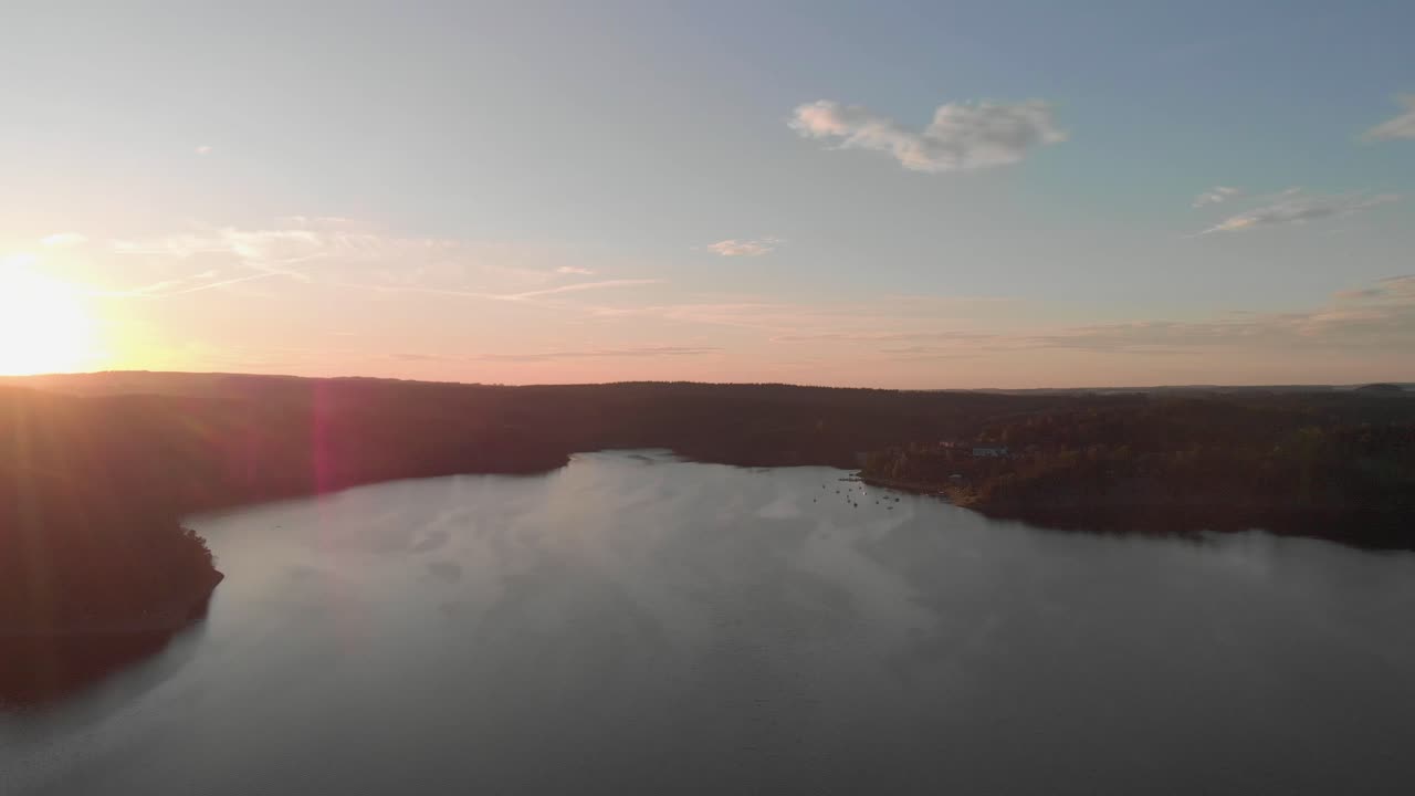 una toma aérea de aspecto profesional de un lago en la puesta de sol naranja rosa, volando directamente hacia el sol