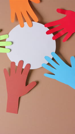 vertical video of hands touching circle made of colourful paper on brown background with copy space
