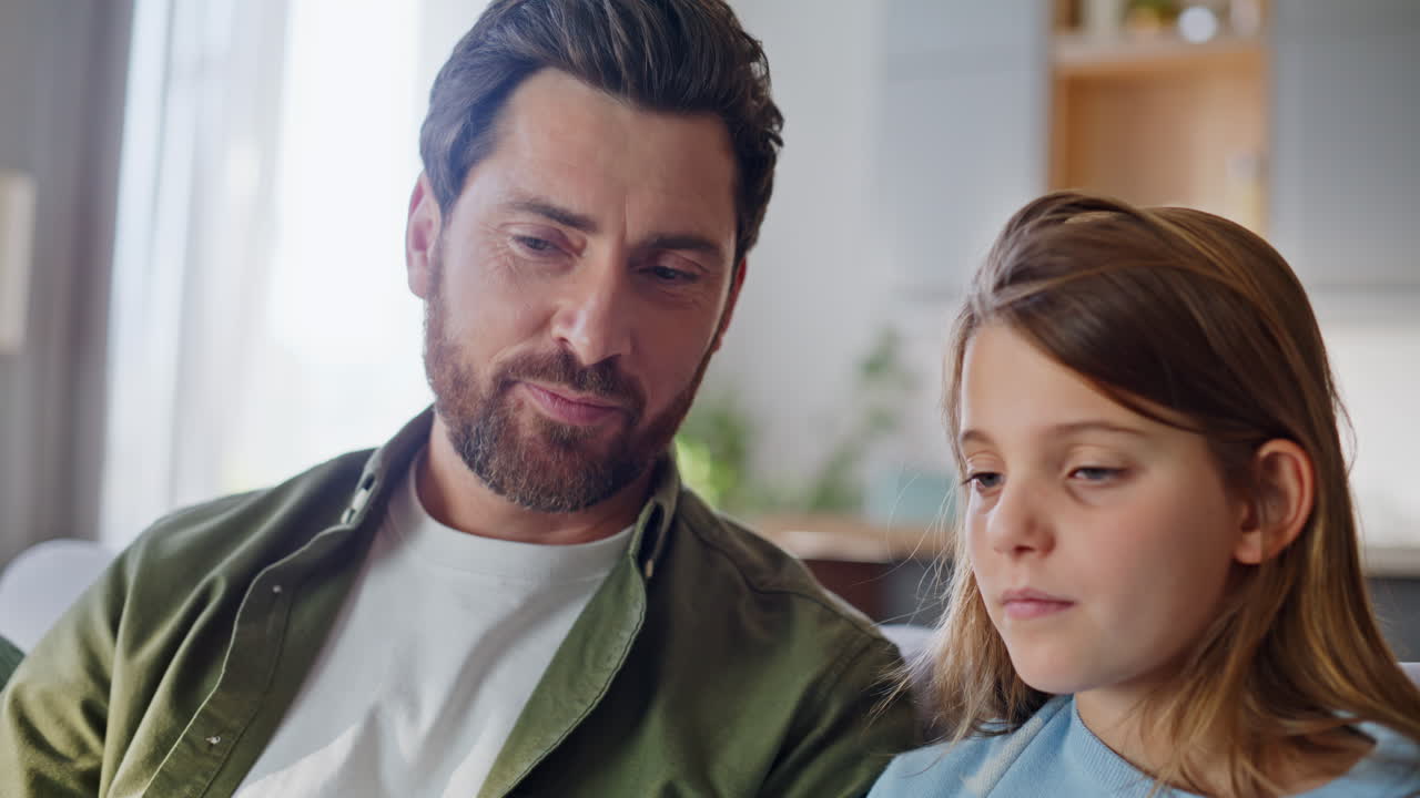 Primo piano di un uomo e una figlia che guardano un cellulare e discutono di contenuti online a casa