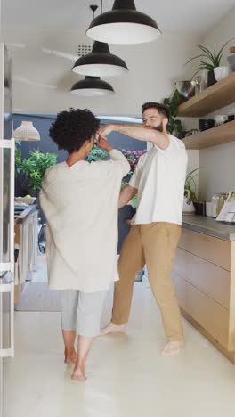 video vertical de una pareja feliz y diversa divirtiéndose bailando juntos en la cocina