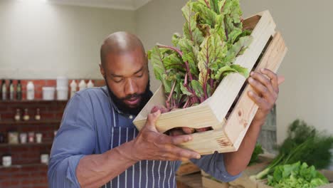 video of happy african american salesman standing with box of vegetables in organic grocery shop