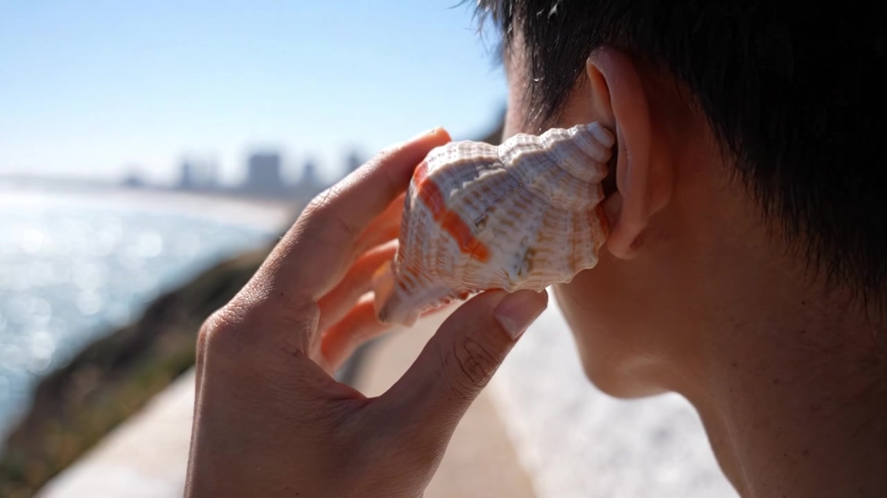 Listening to the Ocean: A Person Holding a Seashell to Their Ear by the Shore, Capturing the Sounds of Nature and Coastal Serenity in a Beautiful Setting