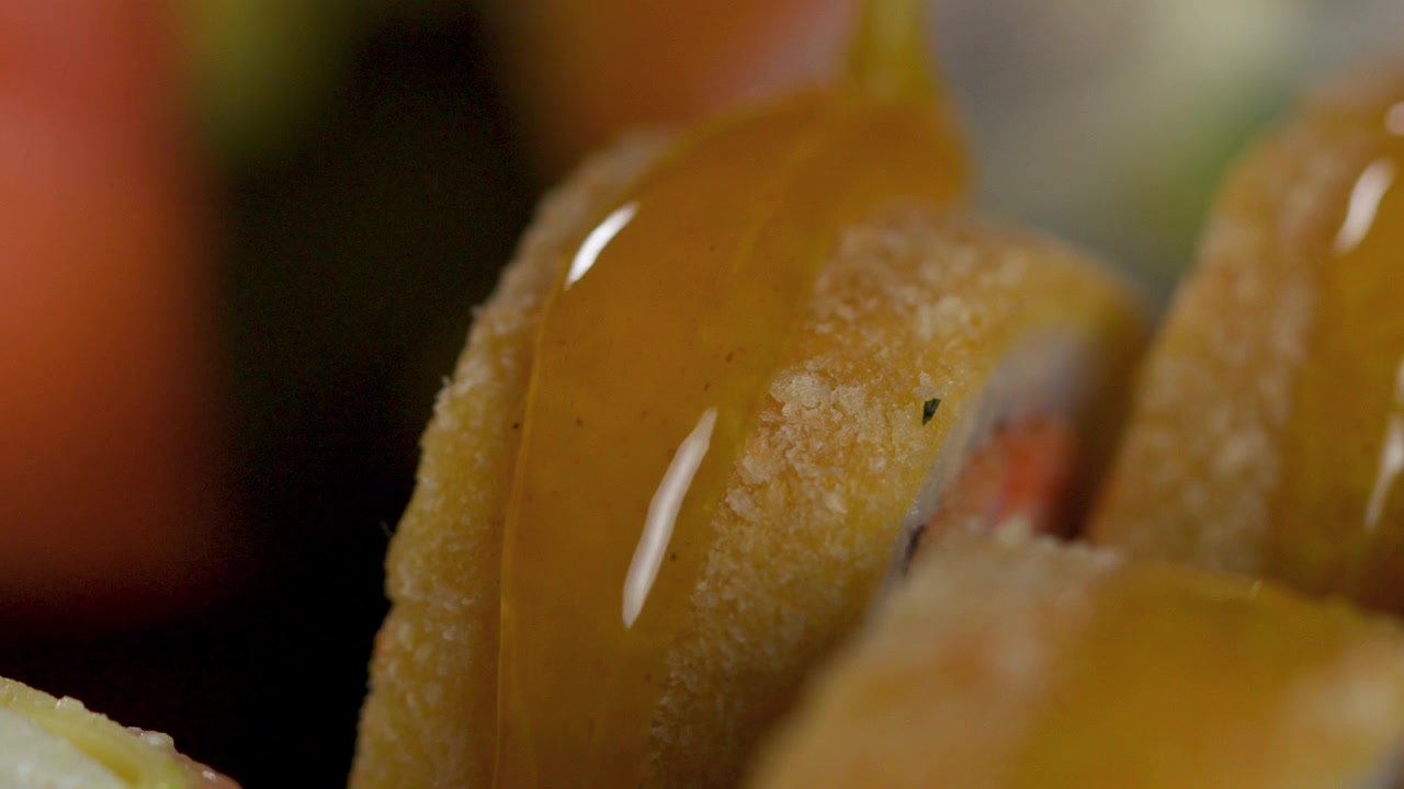 Primissimo piano di salsa al mango versata su un roll di sushi tempura croccante.