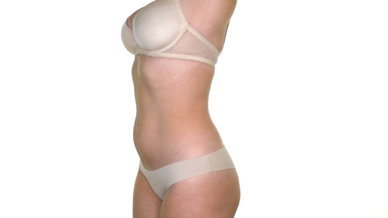 A female model nude coloured bra and underwear, stretching her arms above her head, on a seamless white studio background