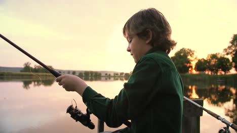 vista de cerca de un adolescente caucásico sentado en el muelle del lago y pescando