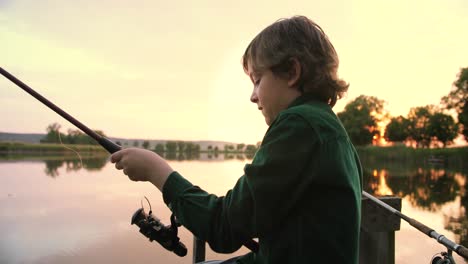 close-up view of a caucasian teen boy sitting on the lake pier and fishing