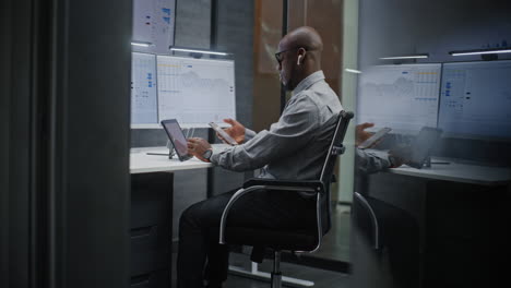 stock exchange trader in wireless headphones having call, monitoring real-time stocks, exchange market charts on multi-monitor desk setup. african american investment agent working. vertical shot.
