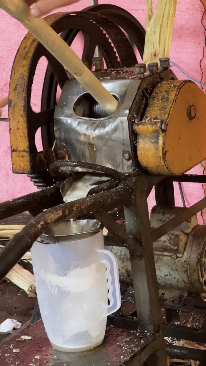 4K close-up of a weathered sugarcane juice machine in a bustling street market. The old, rusty equipment is still working despite its unsanitary appearance, with people eagerly buying juice.