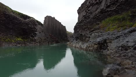 a blue river in studlagil canyon, iceland with basalt rock columns, front view, moving in