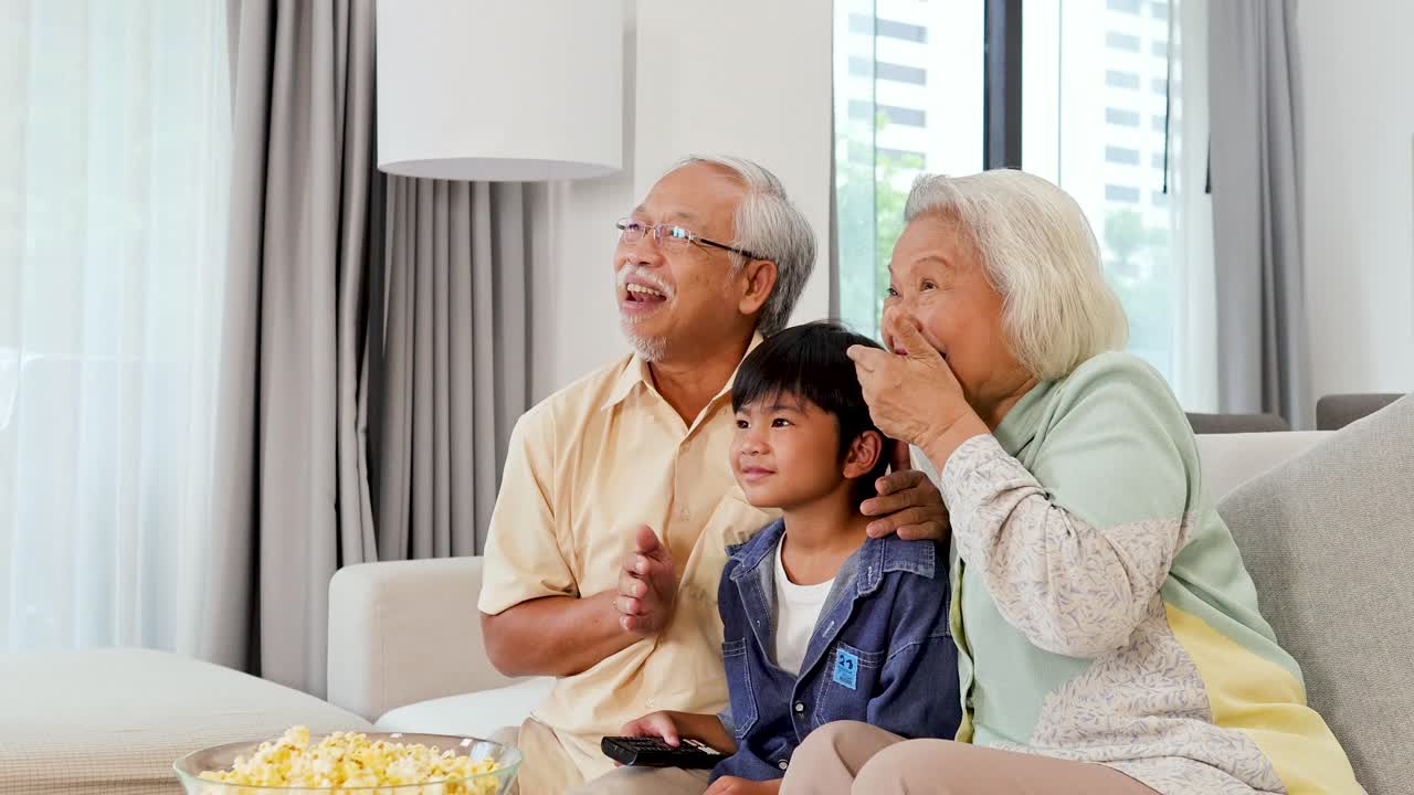 明るいリビングルームでホラー映画を観て、感情的で遊び心のある反応をする祖父母と孫