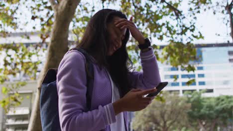 asian woman smiling while using smartphone standing in the park