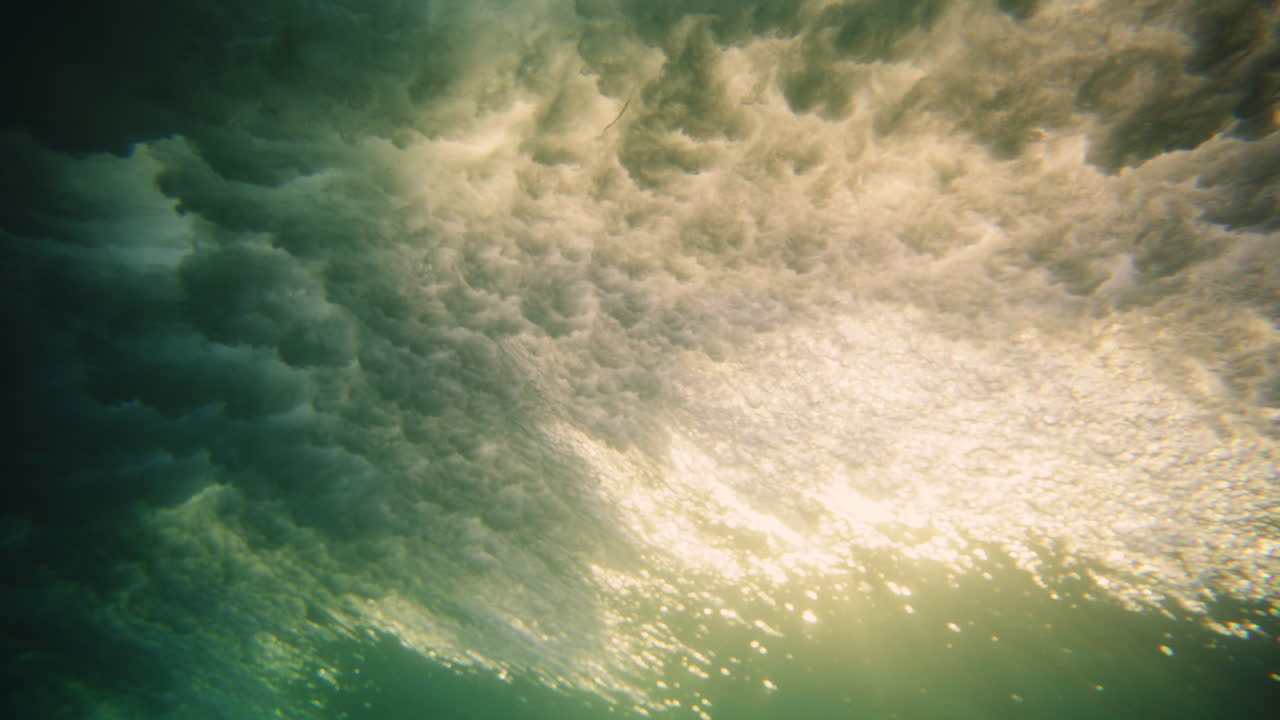 Pan across underwater view of breaking wave crashing on light ray