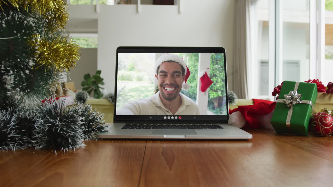 hombre biracial sonriente con sombrero de santa en una videollamada de navidad en una computadora portátil