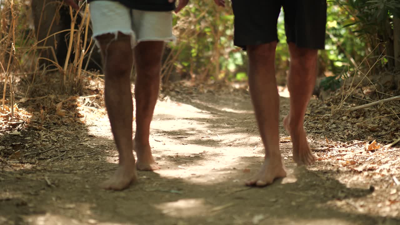 Carrellata di persone a piedi nudi che camminano su un sentiero sterrato illuminato dal sole.