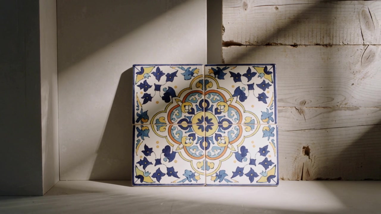 Un raggio di sole si sposta su quattro piastrelle di ceramica su uno scaffale, illuminando il motivo e mostrando la parete in legno