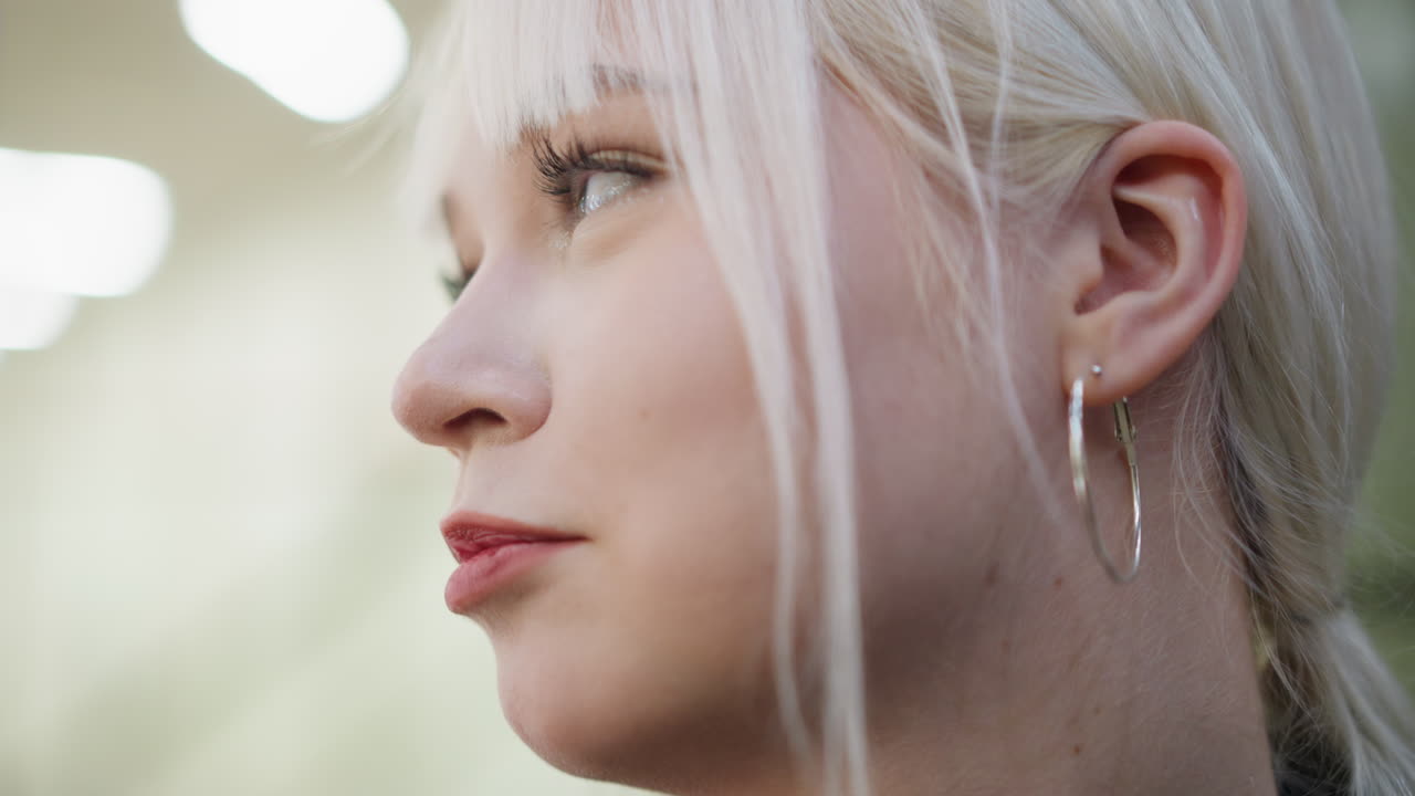 Close up of young blonde woman smiling with eyes closed showing joy and relaxation, soft indoor lighting highlighting her face and expression, natural candid moment with detail of skin texture