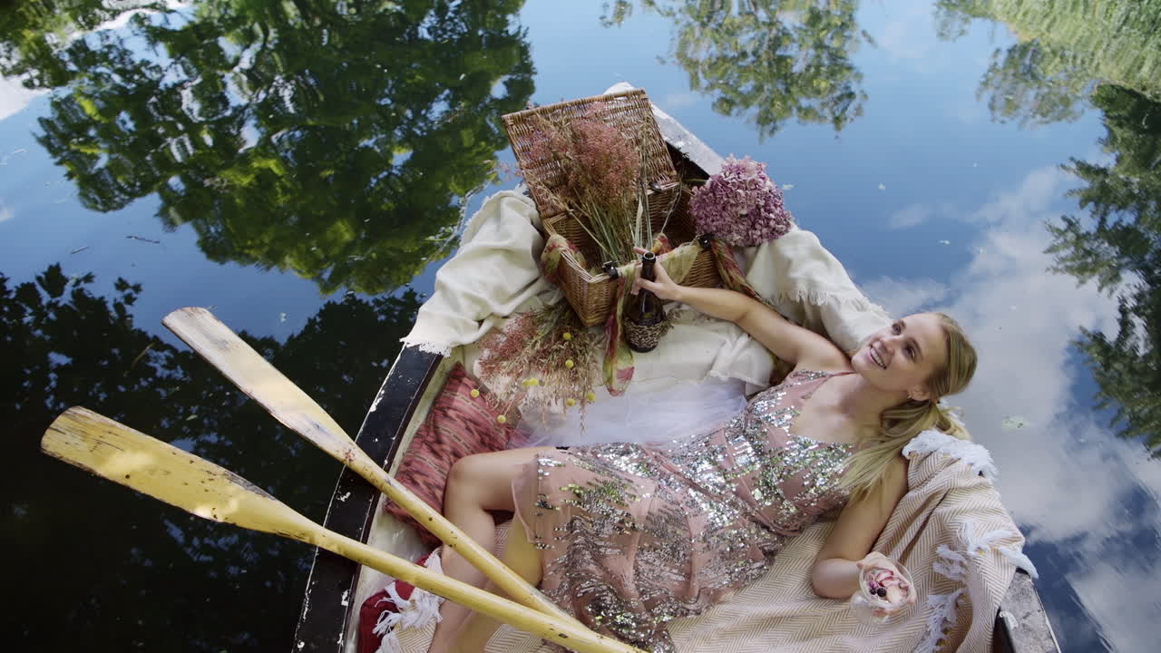 Luxury woman laying in rowboat smiling cheeky at camera and drinking champagne