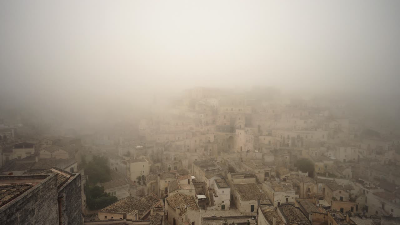 Panoramica lenta verso destra della città vecchia di Matera avvolta nella nebbia, in 4K.