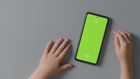 disparo de estudio de arriba de un niño impaciente esperando la pantalla verde del teléfono móvil para cargar 2