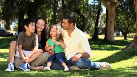 Linda-Familia-Disfrutando-Del-Tiempo-Juntos-Sentados-En-El-Césped