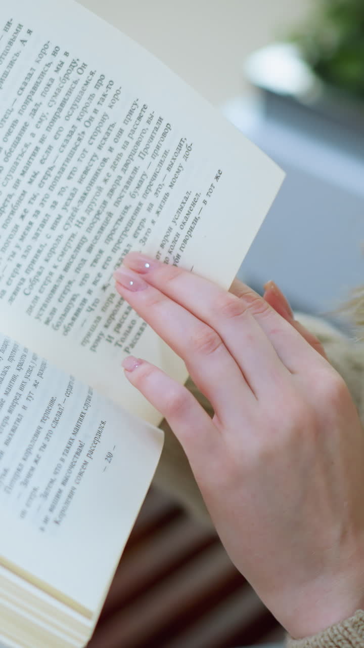 화려한 쇼핑백의 흐릿한 시야를 가진 벤치에 앉아 목걸이를 착용한 화려한 백인 여성이 페이지를 돌리고 있습니다.