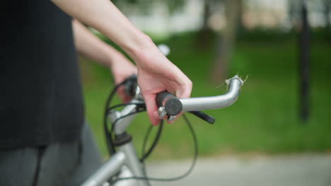 partial view of person in black top walking along side his bicycle bicycle in peaceful pathway, focusing on the hand gripping the bicycle handlebar, the scene is surrounded by greenery