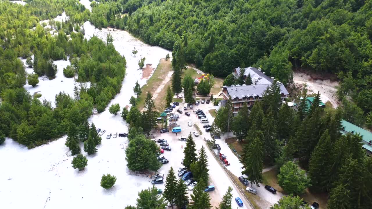 Ilmakuva metsäisestä laaksosta, jossa on rakennuksia ja autoja