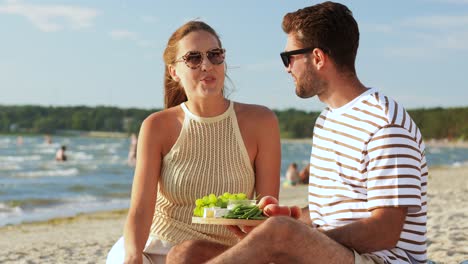 Pareja-Feliz-Con-Comida-Haciendo-Un-Picnic-En-La-Playa.-Concepto-De-Ocio,-Relaciones-Y-Personas.-Pareja-Feliz-Con-Comida-Comiendo-Uvas-Y-Haciendo-Un-Picnic-En-La-Playa.