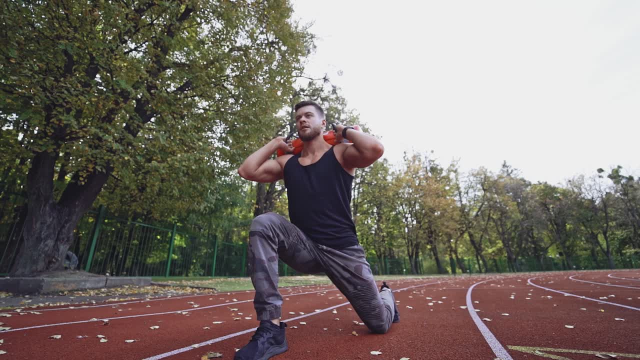 Strong athlete exercising in the stadium. Healthy sportsman doing his workout with heavy weight in the autumn park. Slow motion. View from below.